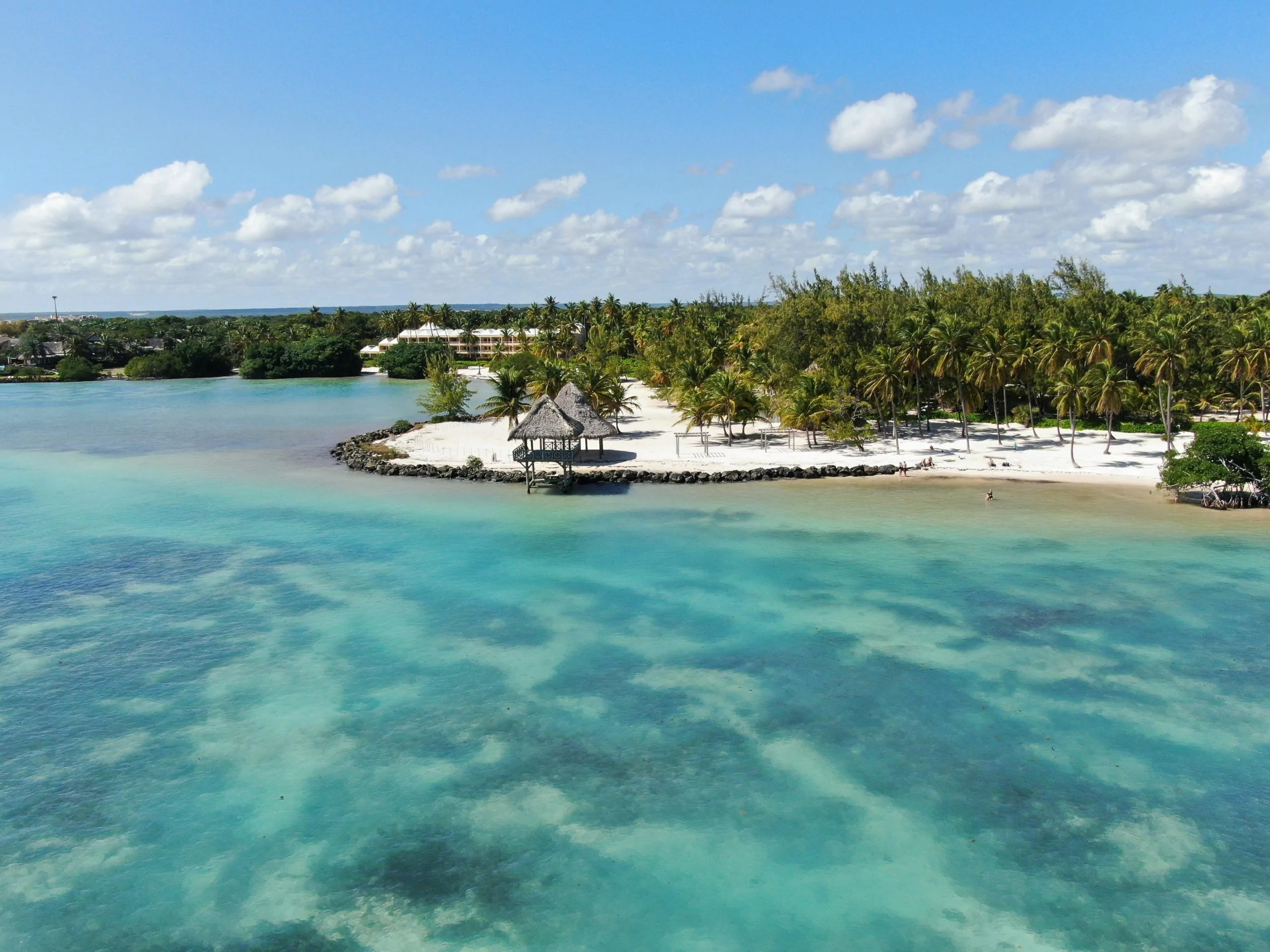 image Vue aérienne d'un lagon turquoise et d'une plage de sable blanc bordée de cocotiers, avec un kiosque en paille sur la pointe