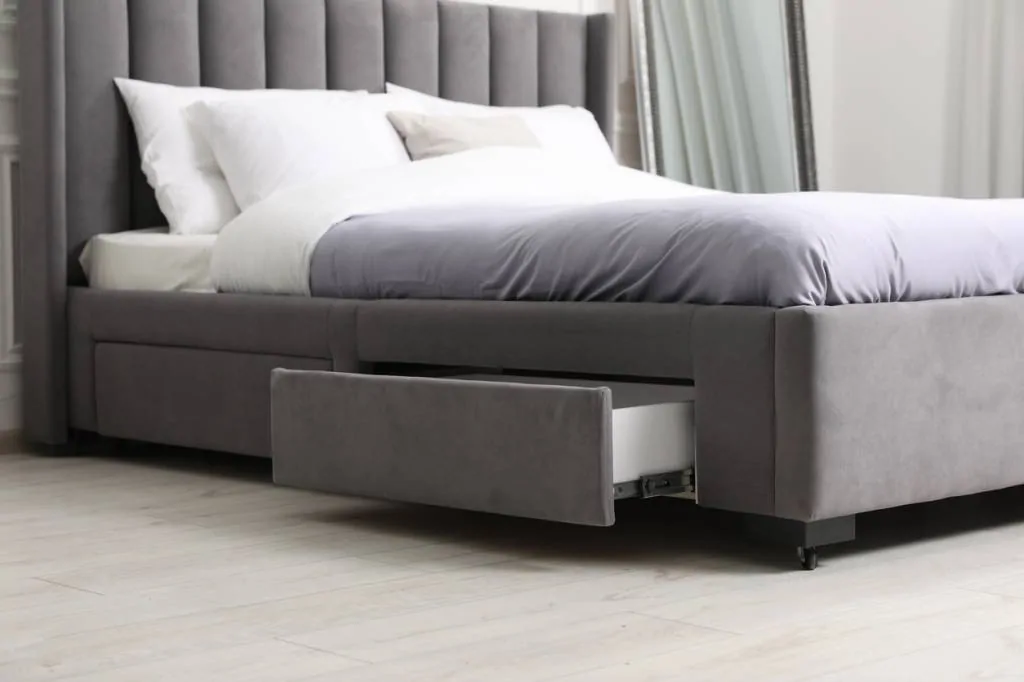 Lit coffre en velours gris à tête de lit matelassée, avec un tiroir de rangement ouvert sous le cadre du sommier