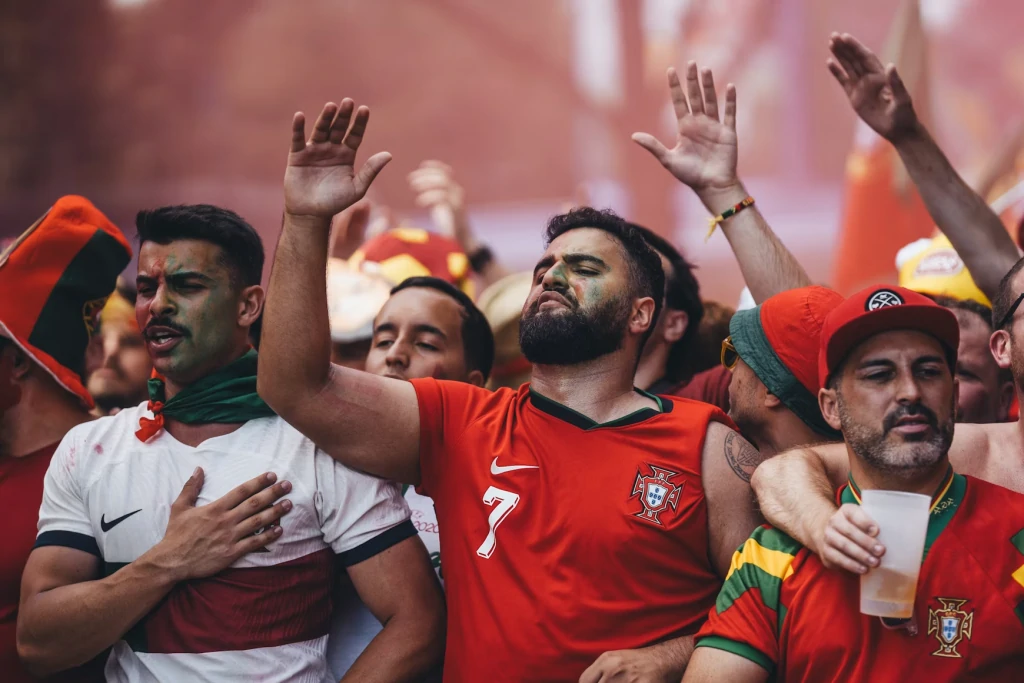 Supporters de football en maillots du Portugal, visages peints et bras levés, chantant au milieu d'une foule