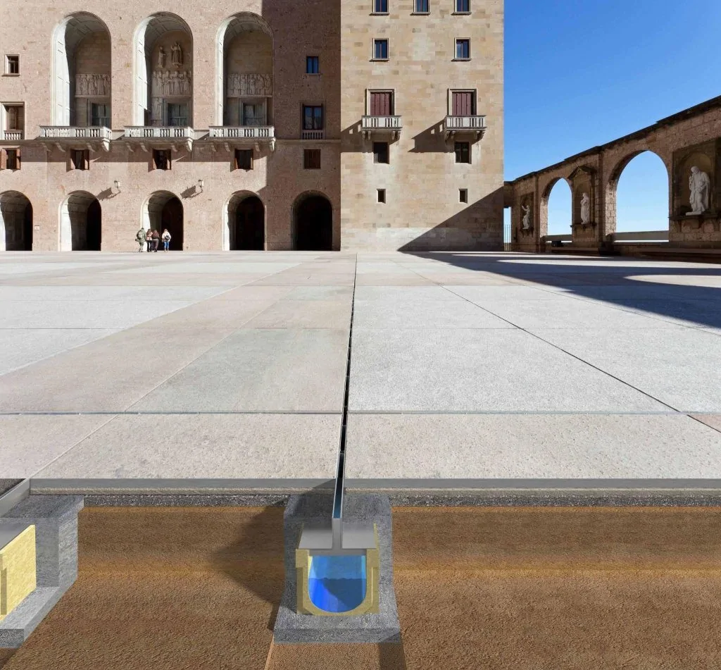 Vue en coupe d'un caniveau à fente discrète noyé dans le béton sous le dallage en pierre d'une grande place