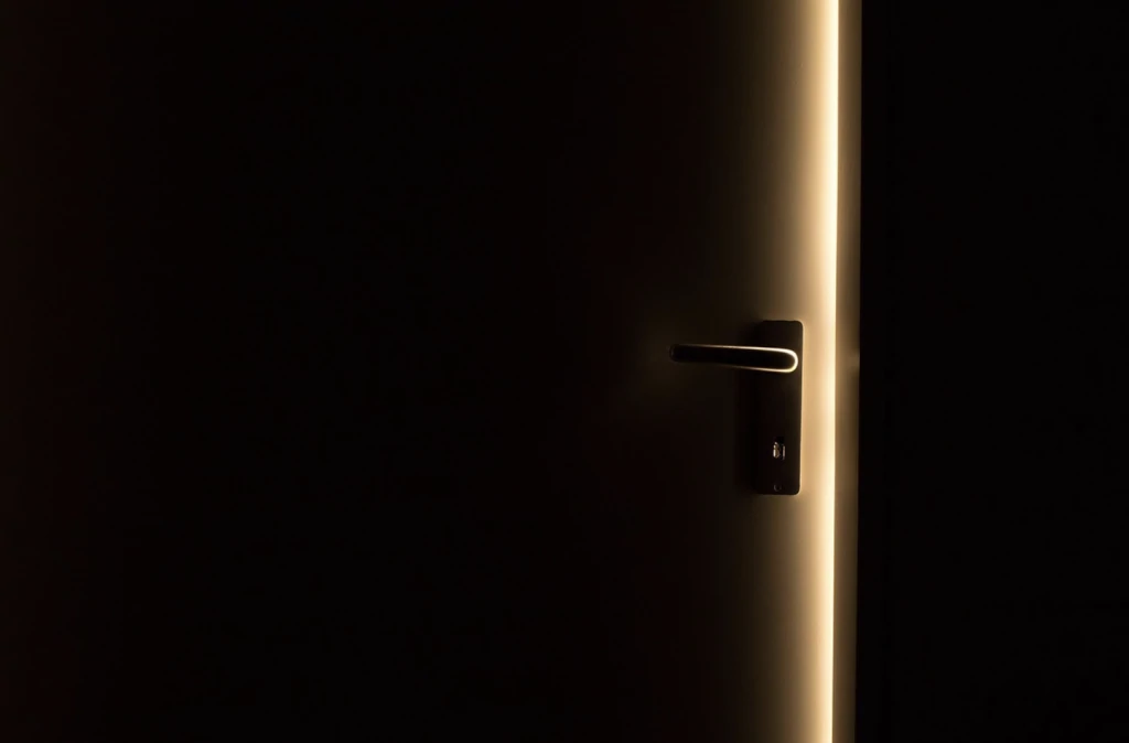 Porte entrouverte dans l'obscurité, poignée et serrure éclairées par un filet de lumière venant de l'autre côté
