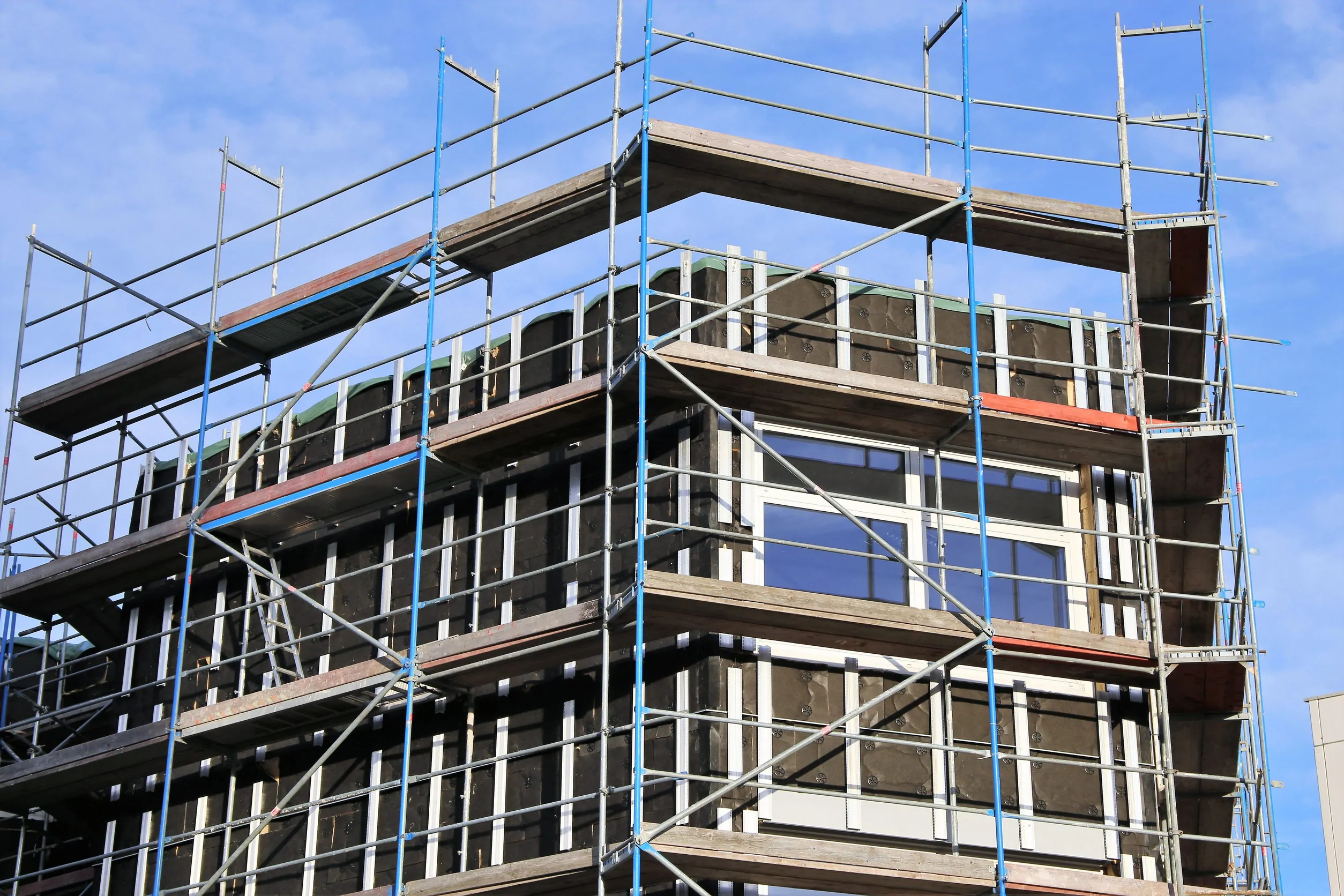 New facade cladding on a building Immeuble sous échafaudage pendant la pose de panneaux de bardage sombres sur sa façade
