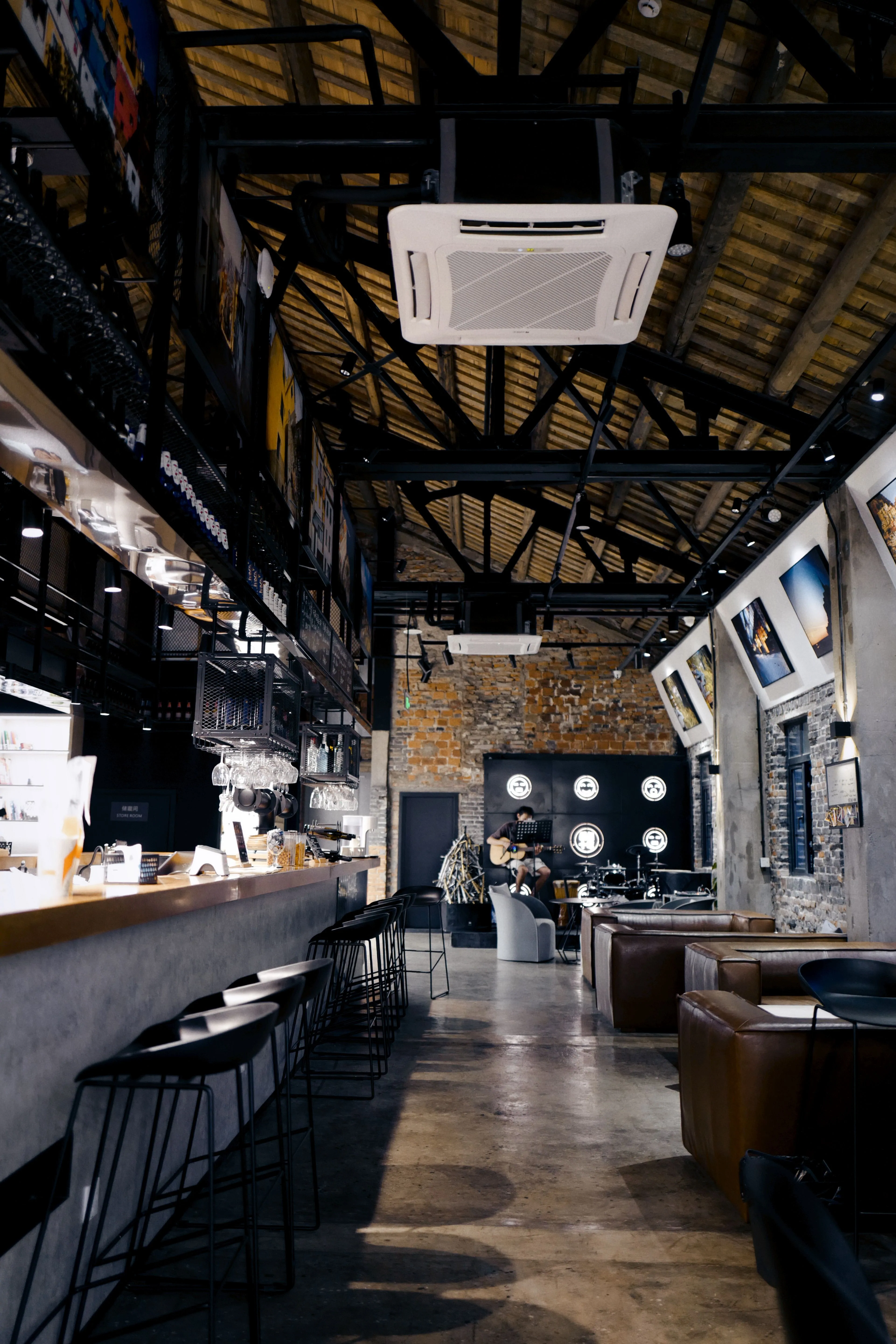 Climatiseur cassette fixé sous la charpente métallique d'un café au style industriel, avec comptoir, tabourets et fauteuils