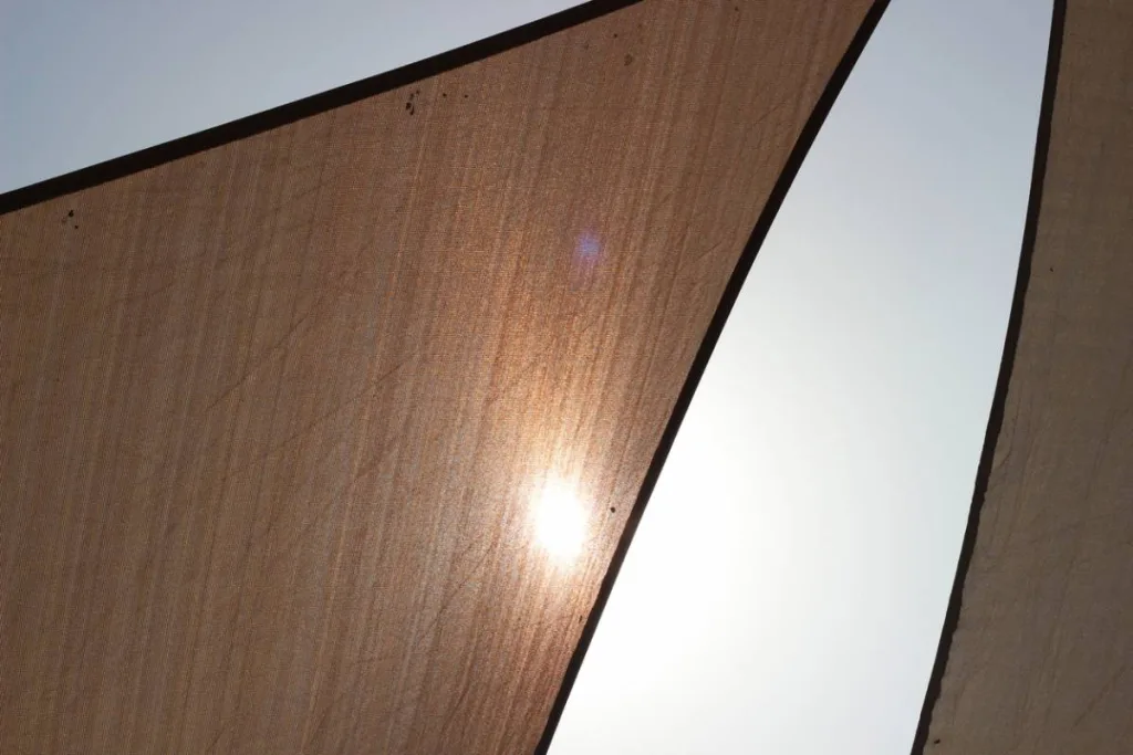 Voiles d'ombrage triangulaires beiges vues par en dessous, le soleil filtrant à travers la toile tendue