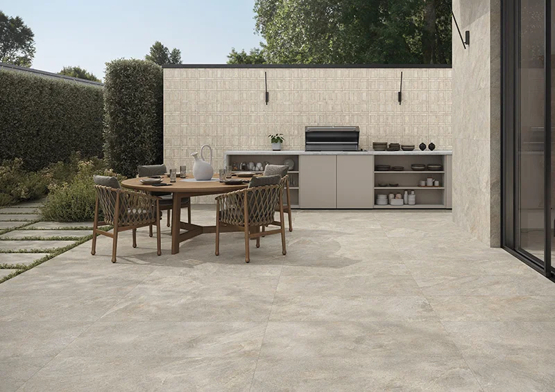 Terrasse dallée de grands carreaux effet pierre avec table ronde, chaises tressées et cuisine d'extérieur