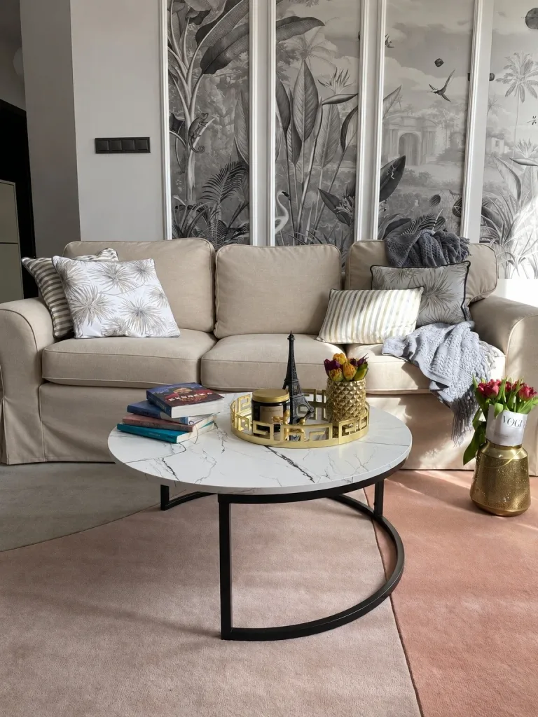 Canapé trois places habillé d'une housse beige, coussins à motif palmes et table basse ronde effet marbre