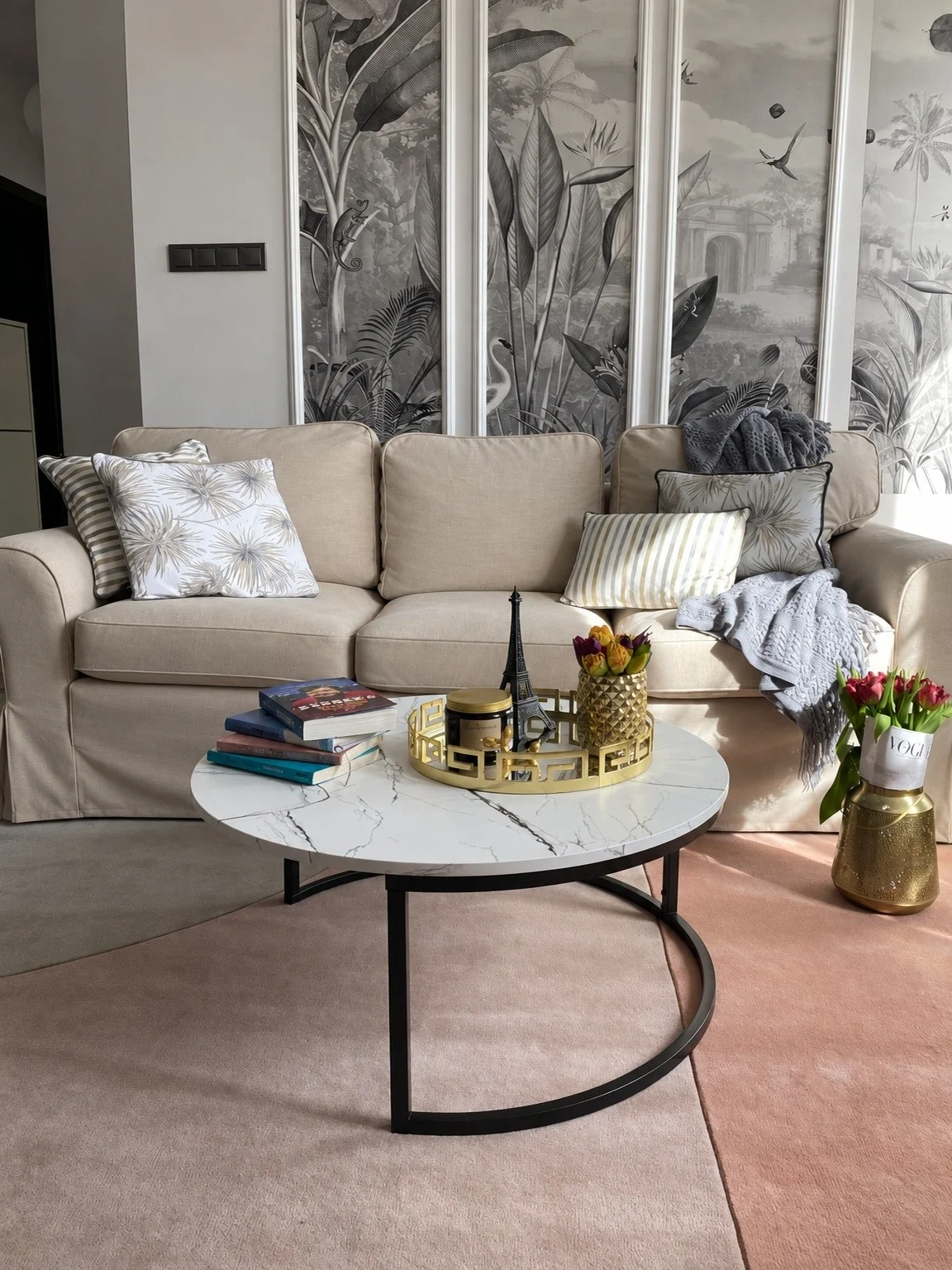Canapé trois places habillé d'une housse beige, coussins à motif palmes et table basse ronde effet marbre